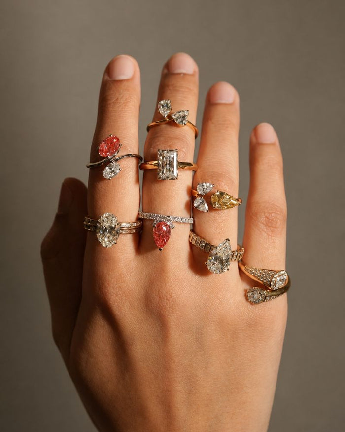 Hand wearing multiple lab grown diamond rings in various colors and cuts.